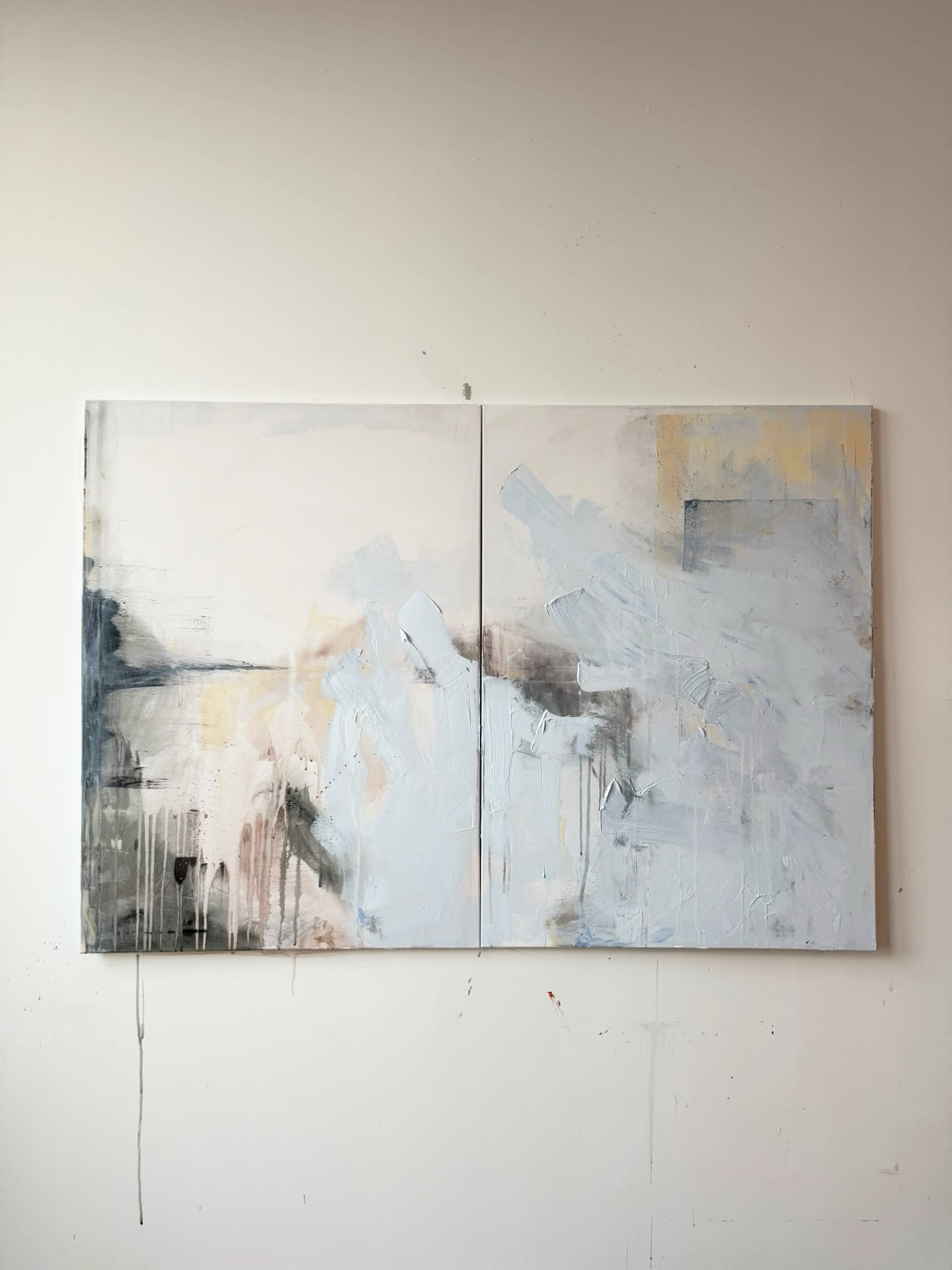 Het tweeluik aan de witte atelierwand. Onder het linkerpaneel loopt een grijze verfdruppel over de muur naar beneden.